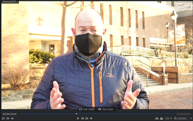 A screenshot of a video frame of the author, shot outside, in front of the library.  